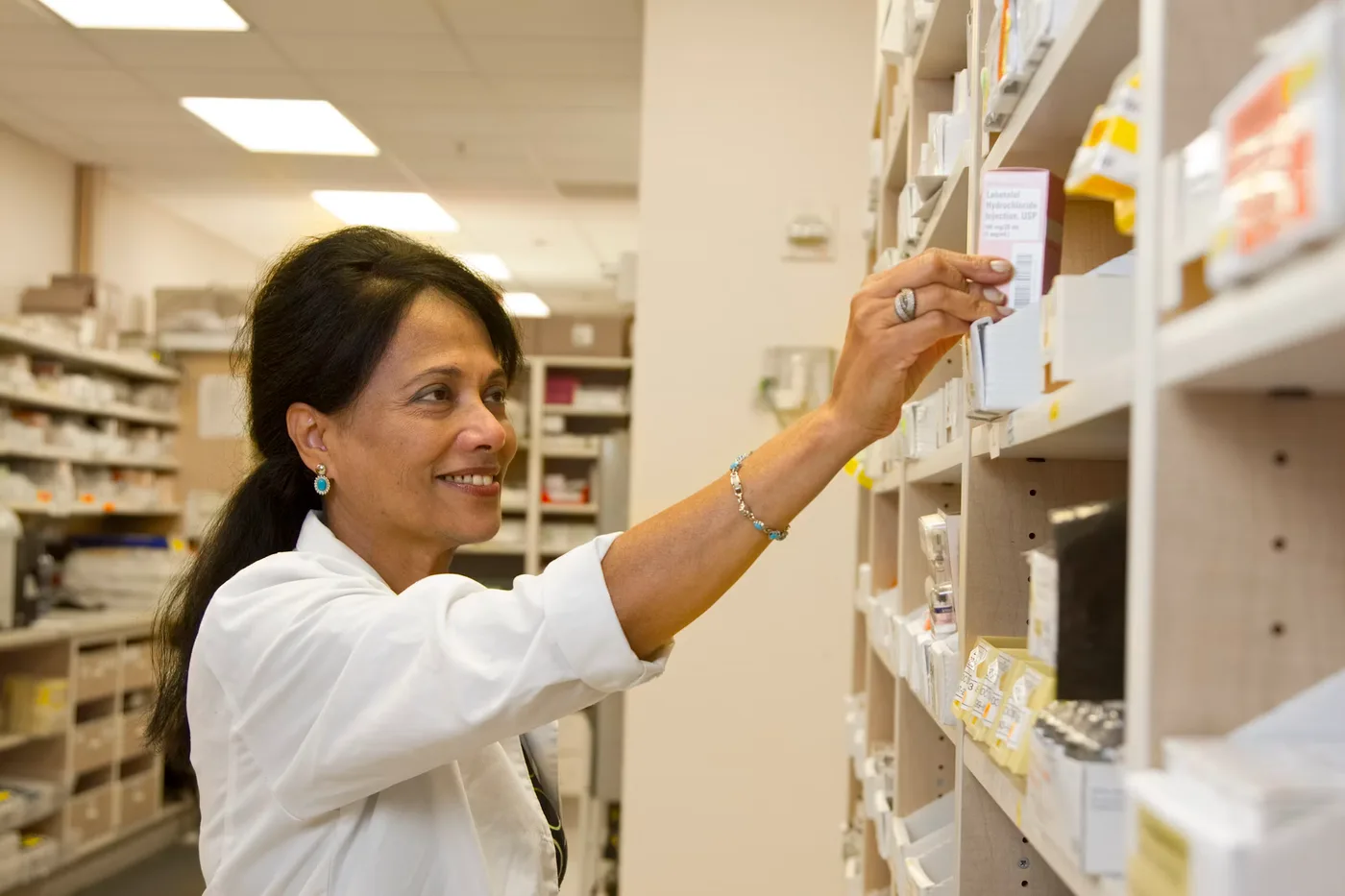 Pharmacienne au comptoir de son officine, devant les rayonnages de médicaments